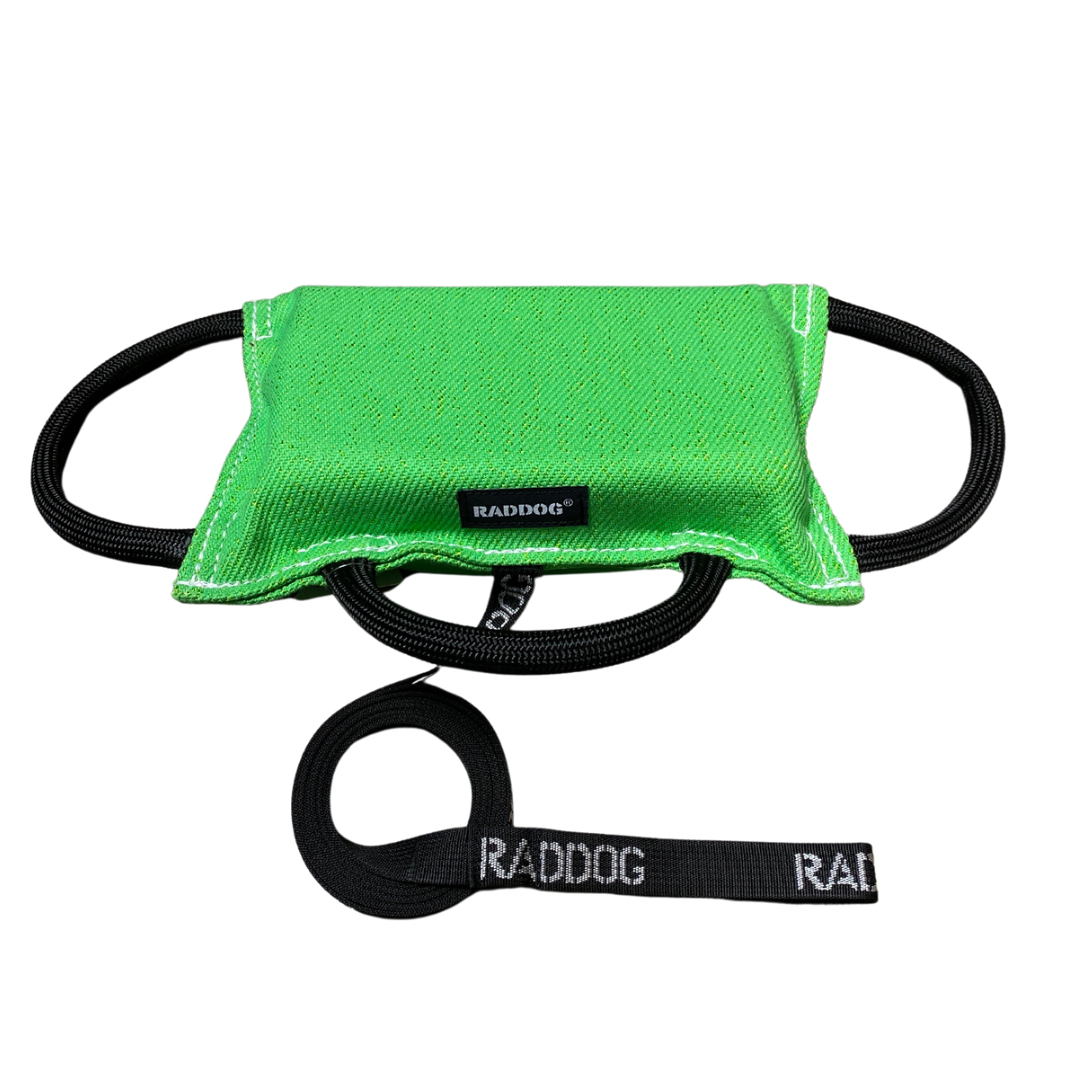 Green dog training bite pad made from durable fabric, featuring reinforced stitching, multiple black loop handles, and a RADDOG logo label, displayed on a white background.