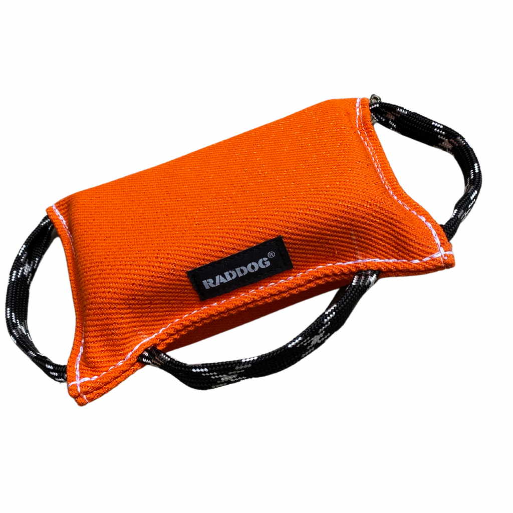 An orange RADDOG bite pad wedge with soft black handles, designed for puppy training.