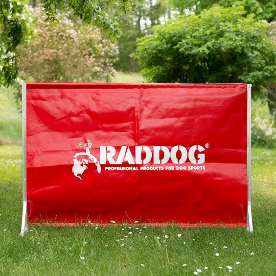 RADDOG transportable dog training jump with red vinyl panel and aluminum frame set up outdoors on grass for IGP obedience training.